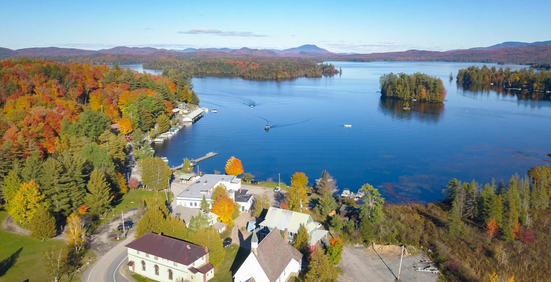 A dock and boat house rest on the edge of a lake with fall foliage surrounding it.
