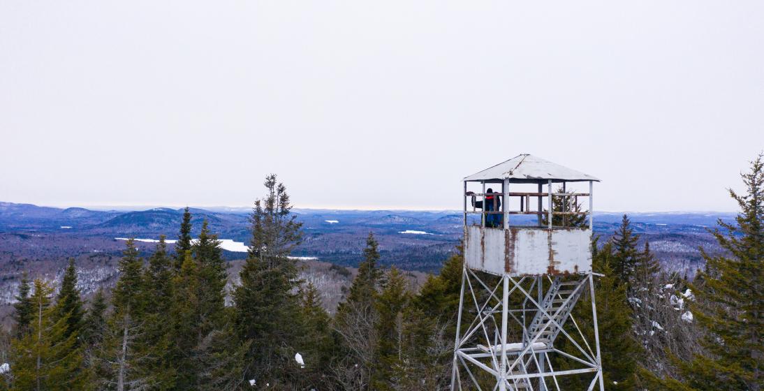 Two people sit in a fire tower in winter above the treeline. 