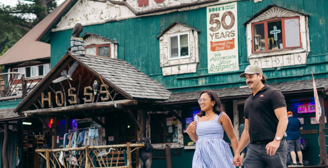 A man and woman walk a cross walk in front of a country store. 