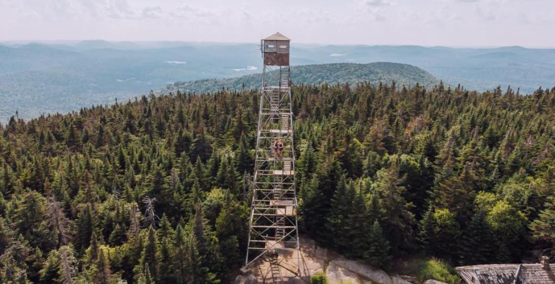 An aerial shot of a fire tower standing above a mountain. 