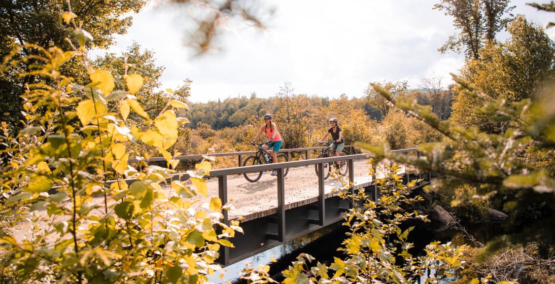 Two women bike across a bridge in the Adirondacks.