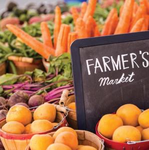 A photo of several baskets filled with various fruits and veggies with a chalk board sign which reads Farmer's Market