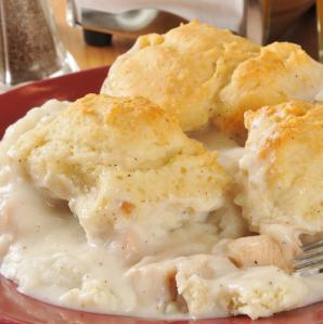 a plate full of chicken and gravy with a few biscuits on top