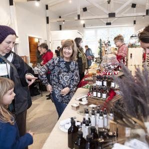 People at an indoor craft fair shopping with artisand behind their display table