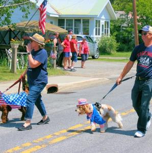 Two men walking marching in the parade with their dogs all dressed patriotically
