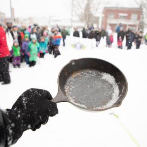a woman holding a frying pan with a crowd watching in the back ground
