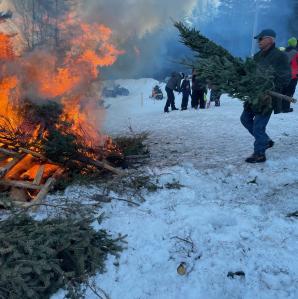 A man throwing another Christmas tree on the bonfire