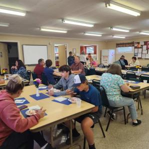 A group of people are sitting at tables in a community hall