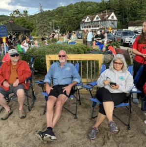 Four people sit in lawn chairs in front of a wooden fence