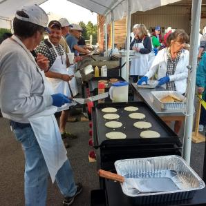 A group of volunteers cook and serve pancakes at an outdoor event.