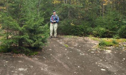 A man standing at the top of a sloped rock feature in the Moose River Plains.