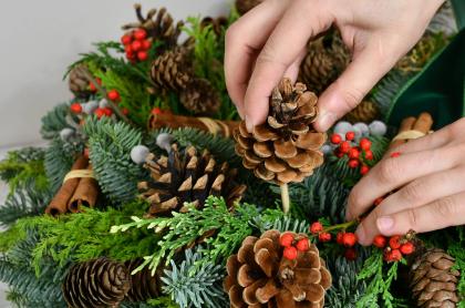 a person adding pines cones to a hand made pine wreath