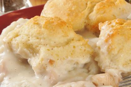 a plate full of chicken and gravy with a few biscuits on top
