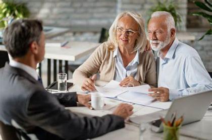 An elderly couple sitting at a table with paperwork in front of them with a man in a suit across the table