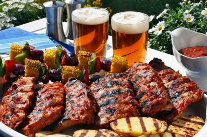 Aplate full of BBQ meat with grilled veggie kabobs and two glasses of beer in the background