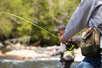 a close up of the fly fishing rod a man is holding while fly fishing with another man fishing in the background