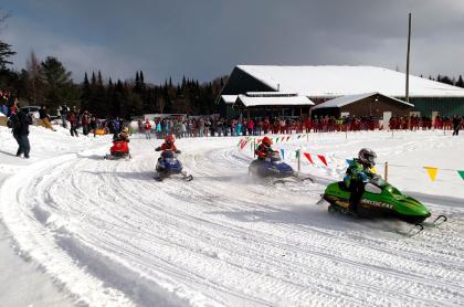 several kids racing mini snowmobiles taking a turn on the snow track
