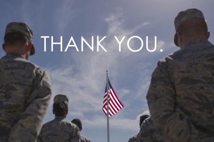 A photo of several military members standing facing an American flag in front of them with the words Thank You. typed in the sky
