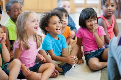Children of pre-k age sitting on the floor enjoying a story read to them