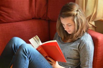A young woman sitting on a couch reading a book