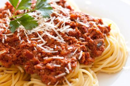 A white plate with spaghetti topped with a red meat sauce and sprinkled with parm cheese.