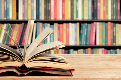A couple of books open and on a table with library books on shelves in the background