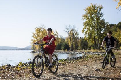  Two boys riding their bikes on a trail along a lake
