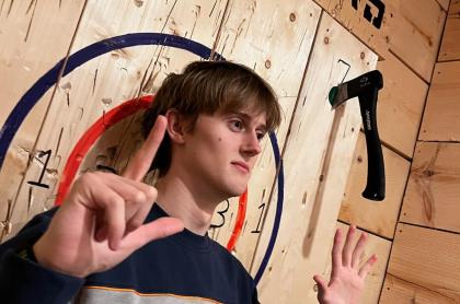 a boy standing infront of the bullseye with his axes in the board