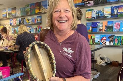 A woman holding a basket that she weaved with a big smile of accomplishment on her face