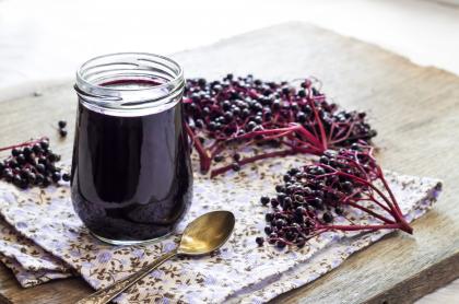 A jar of home made elderberry syrup with a spoon next to it and several bunches of elderberries