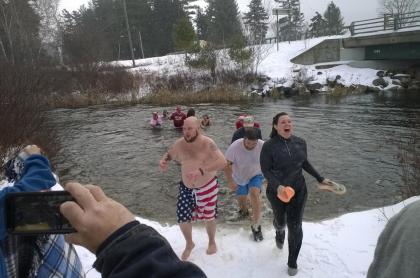 Several people coming back on to a snowy shore after going into the cold winter waters for a polar plunge