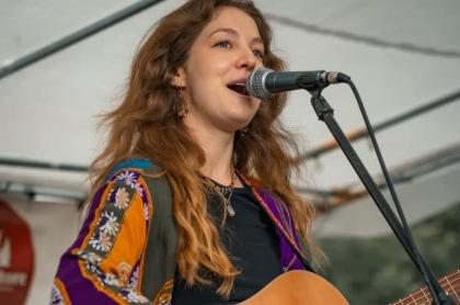 A photo of Jessie singing into a microphone and playing her guitar