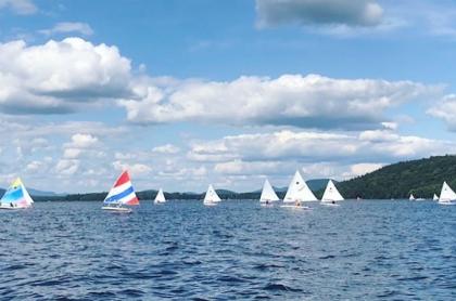 piseco lake with several sailboats on the water with a blue sky above with big puffy white clouds