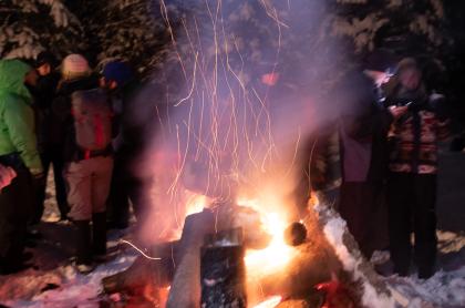 a photo of an outdoors fire at night with people standing in the background