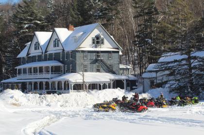 Outside photo of the ADK Hotel in winter with several snowmobiles parked outside