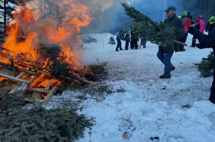 A man throwing another Christmas tree on the bonfire