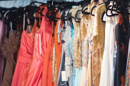 A line of prom and formal dresses hanging on a rack