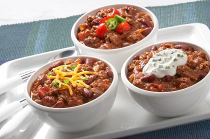 Three small white bowls each with chilli in it with different toppings to garnish each