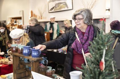 a lady reaching for a hand made pottery mug at a vendor table