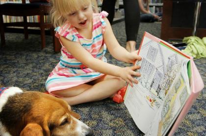 A little girl reading a story to a beagle who is laying on the floor next to her