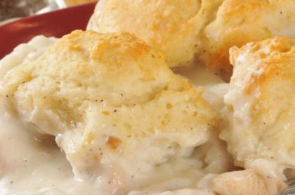 A red plate with chicken in gravy with a few biscuits on the side