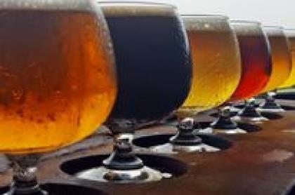 a row of short glasses filled with different types of beer