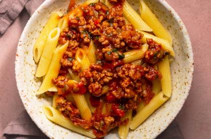a pasta plate full of penne pasta with a red meat sauce on top