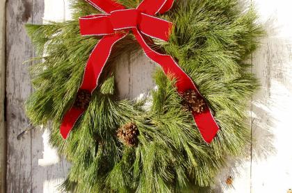 Photo of a hand made wreath using pine branches with a red bow tied to the top