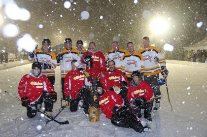 Two teams of hockey players posing for a photo on the ice with snow falling