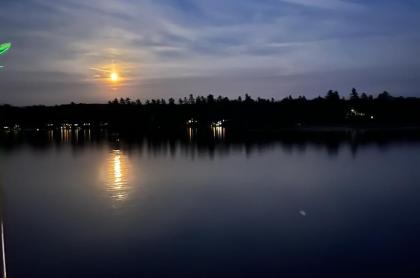 The moon shining brightly in the sky reflecting into Raquette Lake