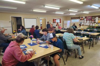 A group of people are sitting at tables in a community hall