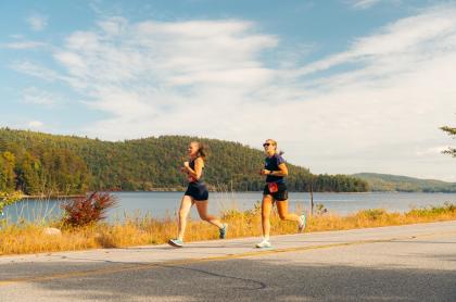Two women run along a paved road during the Adirondack Marathon.