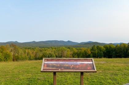 An interpretive sign at a roadside stop overlooking several mountains