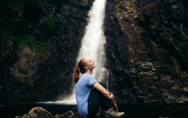 A woman sitting by a waterfall.